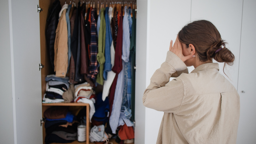 Woman staring at her overloaded wardrobe about to start a wardrobe audit so she can dress for success in her new career.