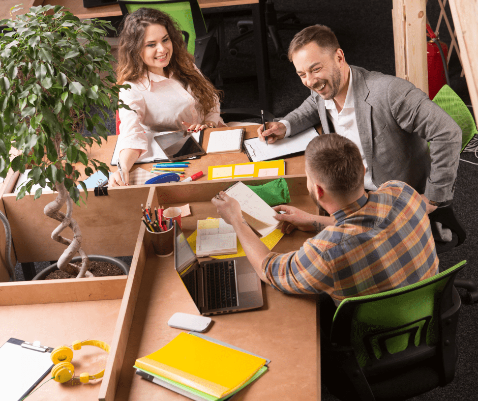 A woman and two men coworking and smiling at a corner desk.