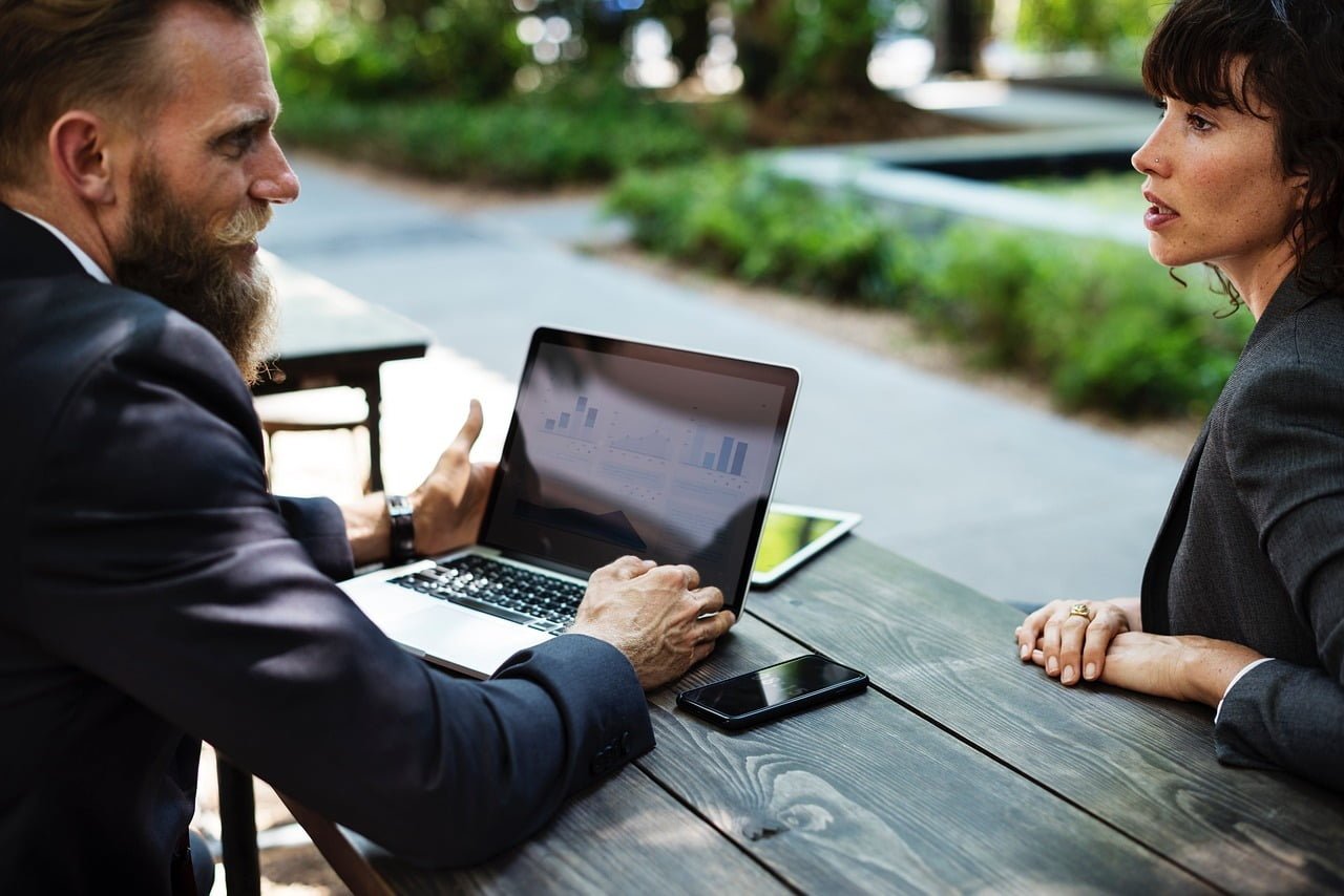 Man at a laptop on an outdoor table with a woman.