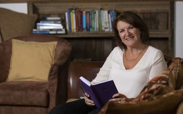 Louise Jenner sitting on a sofa holding a book ready to tell: My Story - How I left My Job.