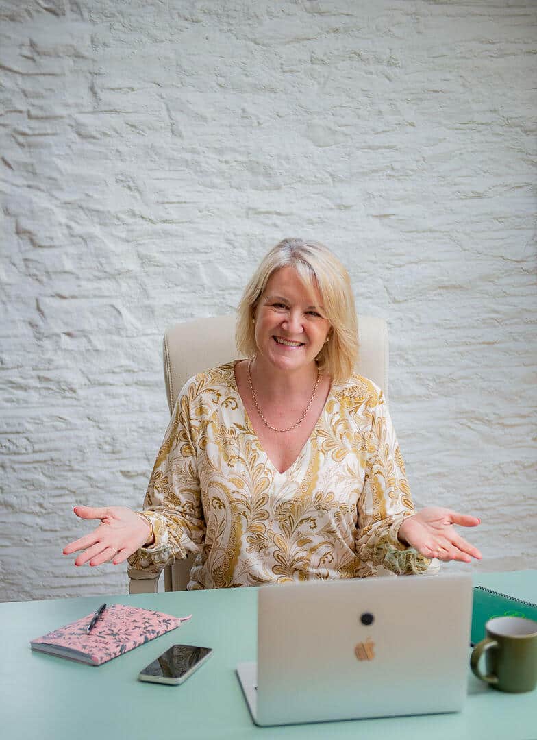 Louise Jenner is sitting at her desk with her arms out and palms up, inviting questions.