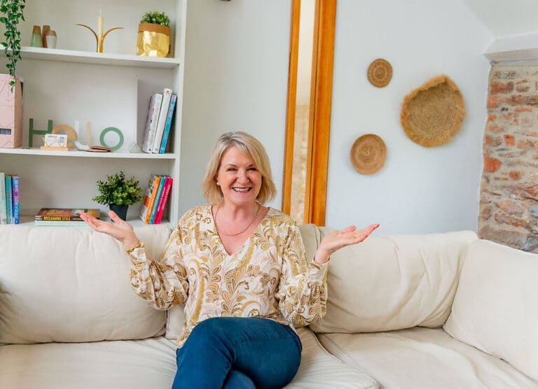 Louise Jenner sitting on a cream leather sofa with her arms slightly raised, palms to the sky.