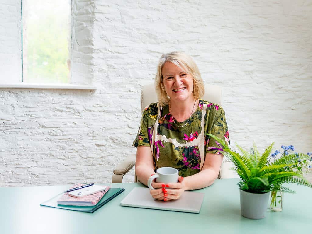 Louise Jenner sitting at a desk with a mug in her hands, taking a break between career coaching clients.